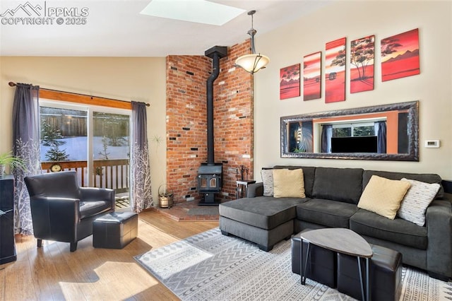 living room featuring light hardwood / wood-style flooring, vaulted ceiling with skylight, and a wood stove