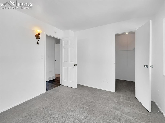 unfurnished bedroom with dark colored carpet, a closet, and a spacious closet