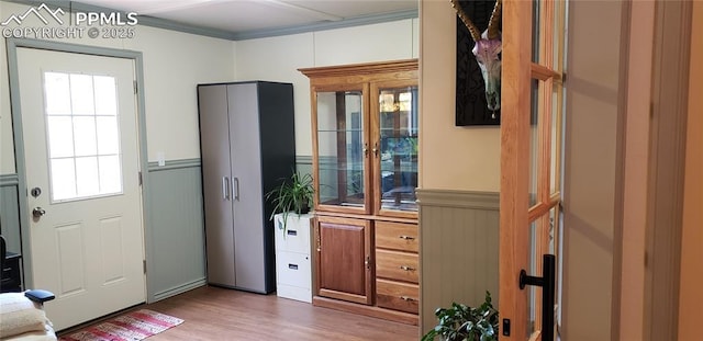 doorway to outside with wainscoting, crown molding, and wood finished floors