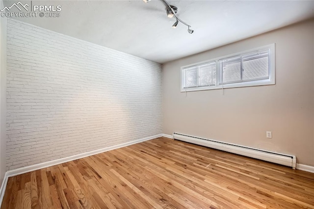 empty room with brick wall, track lighting, baseboard heating, and light hardwood / wood-style floors