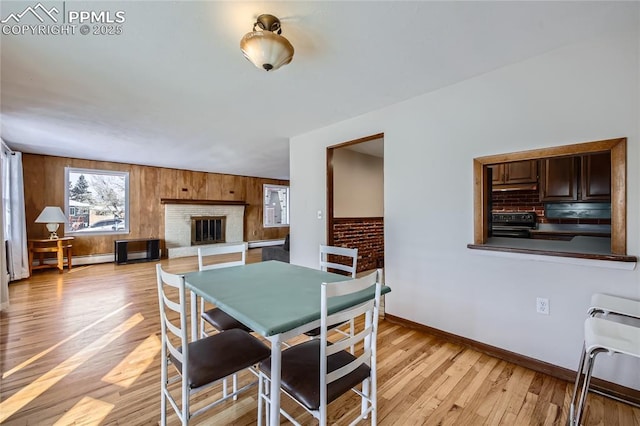 dining space featuring heating unit, wooden walls, a baseboard heating unit, a brick fireplace, and light hardwood / wood-style flooring