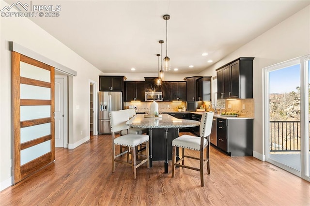 kitchen with appliances with stainless steel finishes, a kitchen island, tasteful backsplash, and pendant lighting