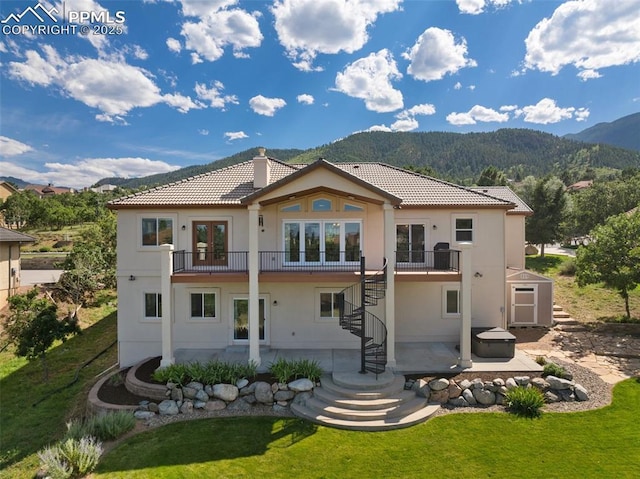 rear view of house with a lawn, a mountain view, french doors, a patio, and a balcony