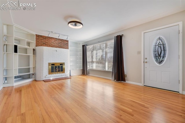 unfurnished living room with rail lighting, a brick fireplace, and light hardwood / wood-style flooring