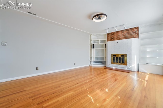 unfurnished living room featuring a brick fireplace, hardwood / wood-style flooring, and track lighting