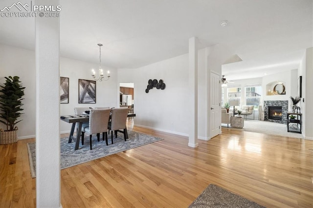 dining room with a stone fireplace, ceiling fan with notable chandelier, and light wood-type flooring