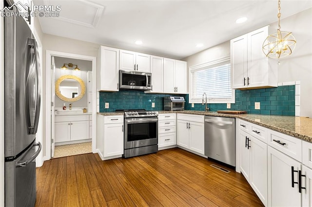 kitchen featuring hardwood / wood-style floors, white cabinetry, pendant lighting, stainless steel appliances, and light stone countertops