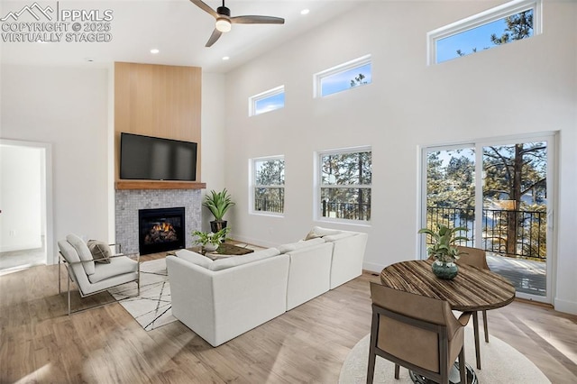 living room with ceiling fan, a high ceiling, and light wood-type flooring