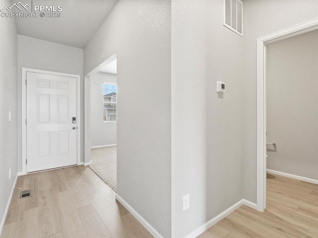 hallway featuring visible vents, baseboards, and light wood finished floors