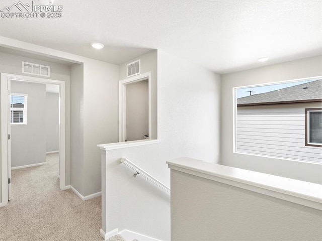 corridor featuring visible vents, light carpet, plenty of natural light, and an upstairs landing