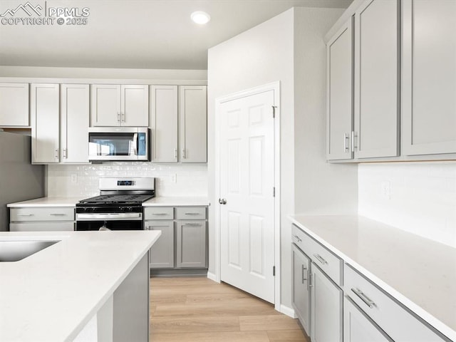 kitchen featuring stainless steel appliances, backsplash, light wood-style flooring, and light countertops