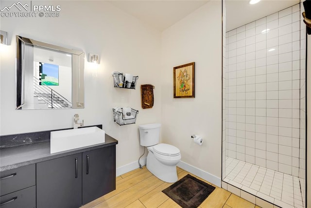 bathroom with a tile shower, vanity, wood-type flooring, and toilet