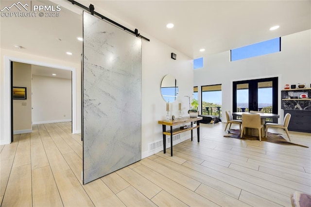 hall featuring a barn door, a towering ceiling, light wood-type flooring, and french doors