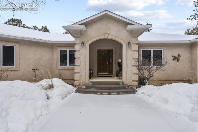 snow covered property entrance featuring stucco siding