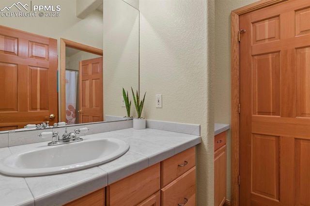 full bath with a textured wall and vanity