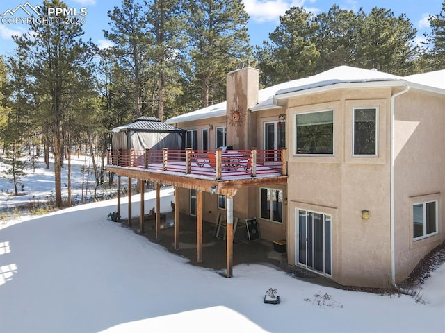 snow covered rear of property featuring a chimney, a deck, and stucco siding