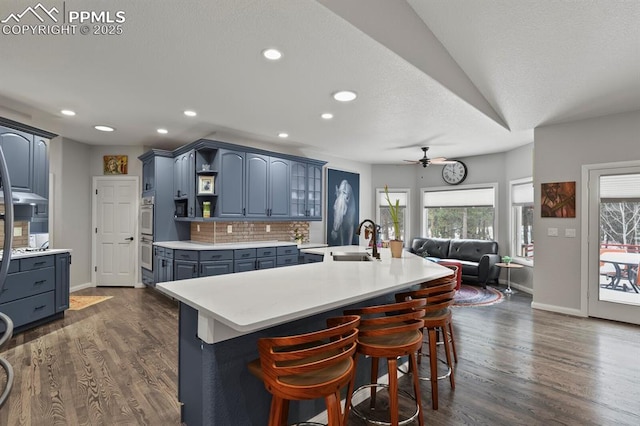 kitchen with blue cabinets, dark wood-style flooring, a sink, light countertops, and tasteful backsplash