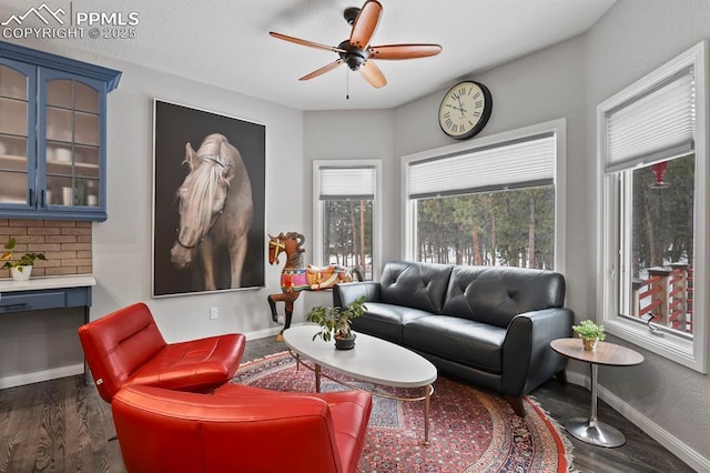 living area with dark wood-type flooring, a ceiling fan, and baseboards