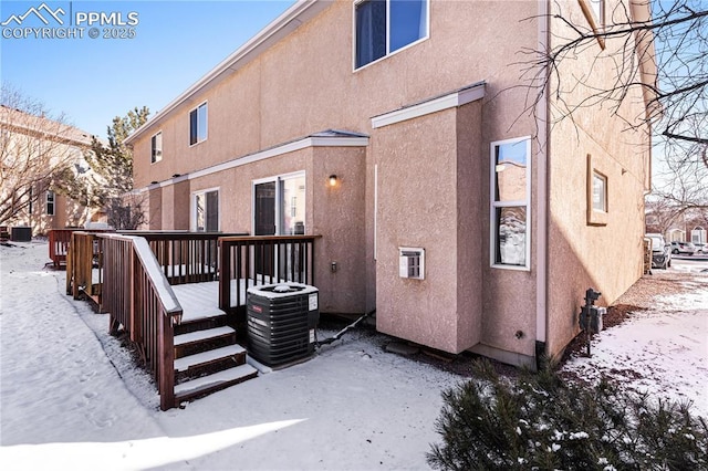 snow covered house with a wooden deck and central AC unit