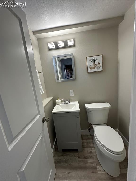 half bath with toilet, a textured ceiling, wood finished floors, and vanity