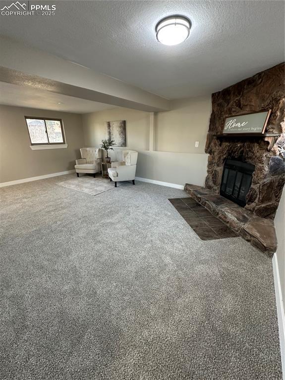 unfurnished living room with carpet, baseboards, a textured ceiling, and a stone fireplace