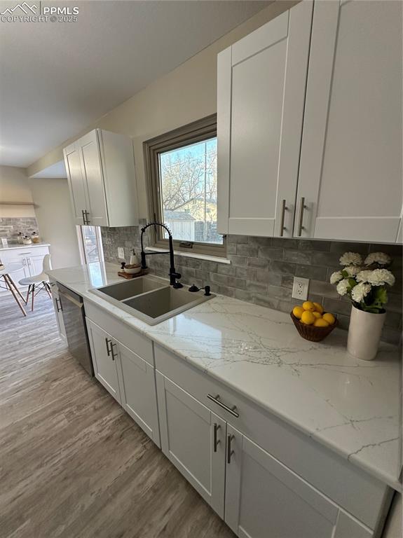 kitchen with stainless steel dishwasher, backsplash, a sink, and light wood-style floors