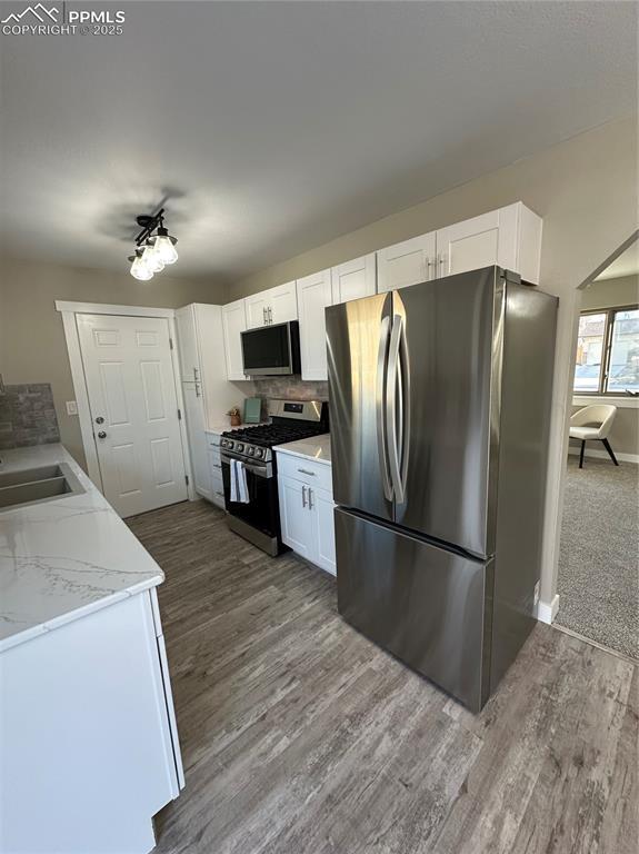 kitchen featuring stainless steel appliances, wood finished floors, a sink, and white cabinets