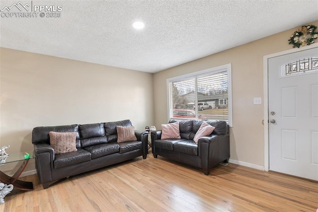 living area with baseboards, light wood-type flooring, and a textured ceiling