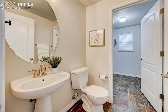 bathroom featuring toilet, stone finish floor, baseboards, and a sink