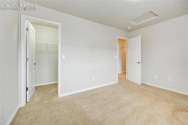 unfurnished bedroom featuring attic access, a walk in closet, carpet flooring, and baseboards