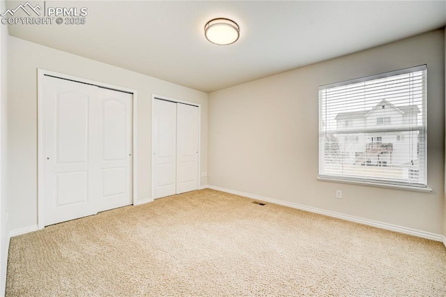 unfurnished bedroom with visible vents, baseboards, two closets, and carpet flooring