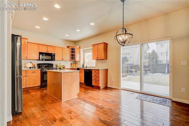 kitchen with black appliances, light wood finished floors, decorative backsplash, and an inviting chandelier