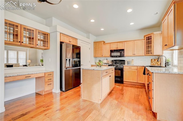 kitchen with light wood finished floors, a kitchen island, black appliances, light brown cabinets, and a sink