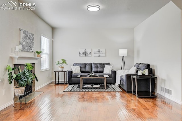 living area with a tile fireplace, visible vents, baseboards, and hardwood / wood-style flooring