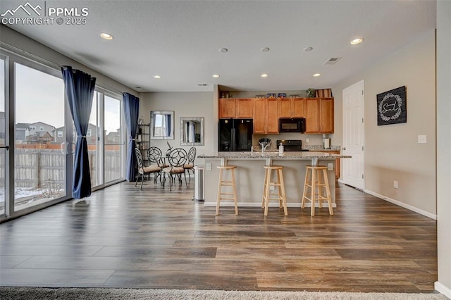 kitchen featuring a breakfast bar, dark hardwood / wood-style floors, light stone countertops, black appliances, and a center island with sink