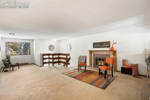 living area featuring visible vents, carpet flooring, a textured ceiling, and a tiled fireplace