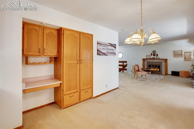 kitchen with a notable chandelier, light carpet, baseboards, hanging light fixtures, and a tiled fireplace