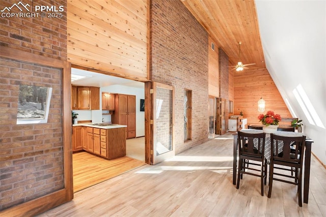 dining room with ceiling fan, high vaulted ceiling, light wood finished floors, and brick wall