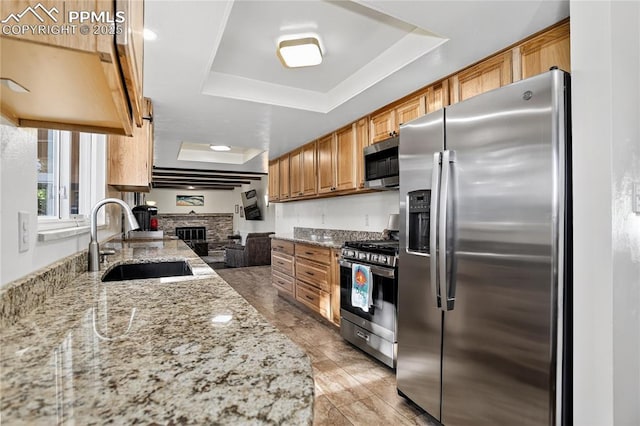 2113 Woodburn St, Colorado Springs, CO 80906 - kitchen featuring appliances with stainless steel finishes, a raised ceiling, light stone countertops, a fireplace, and brown cabinets
