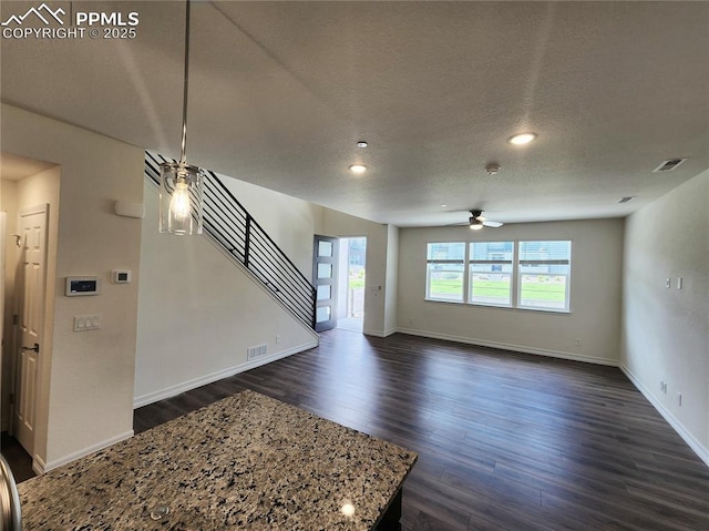 unfurnished living room featuring visible vents, ceiling fan, dark wood-style flooring, stairs, and a textured ceiling