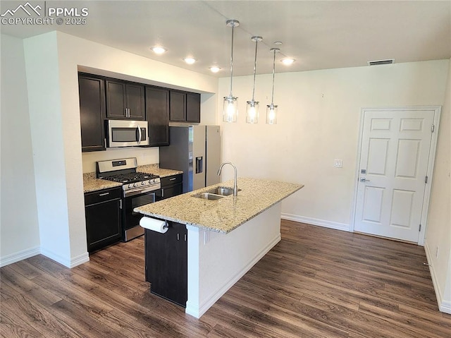 kitchen with dark wood-style flooring, appliances with stainless steel finishes, a sink, an island with sink, and baseboards