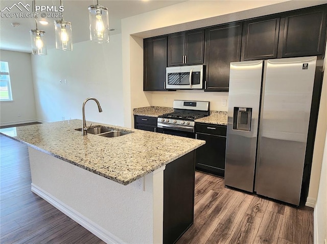 kitchen featuring light stone counters, stainless steel appliances, a kitchen island with sink, a sink, and wood finished floors