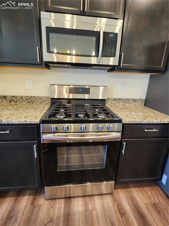 kitchen featuring appliances with stainless steel finishes, light stone counters, and wood finished floors