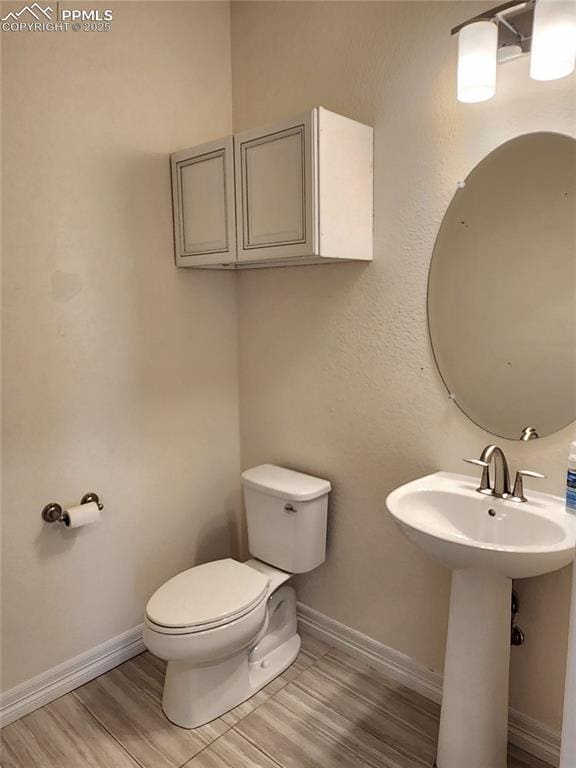 half bathroom with a sink, wood finished floors, toilet, and baseboards