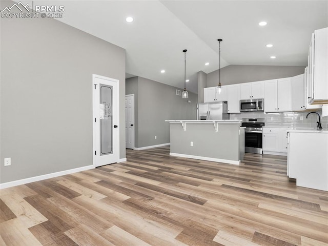 kitchen with appliances with stainless steel finishes, light countertops, white cabinetry, a kitchen island, and vaulted ceiling