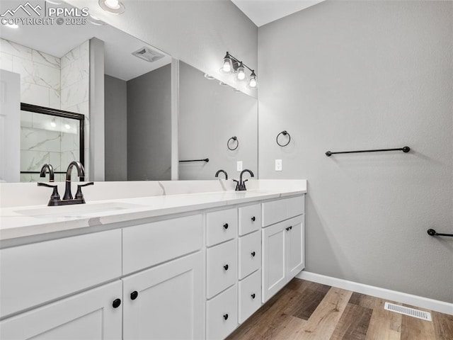 full bathroom with double vanity, wood finished floors, visible vents, a sink, and a marble finish shower