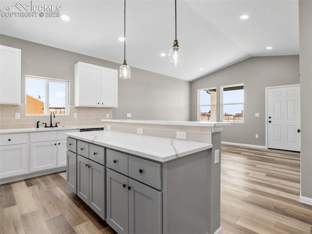 kitchen featuring a sink, hanging light fixtures, gray cabinetry, light stone counters, and white cabinets