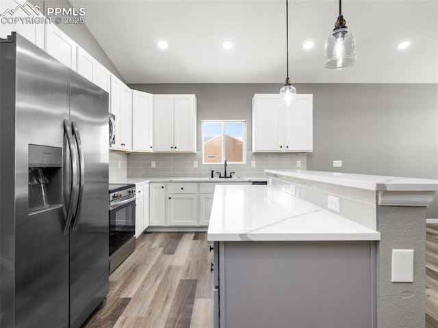 kitchen featuring stainless steel appliances, a sink, decorative light fixtures, white cabinetry, and backsplash