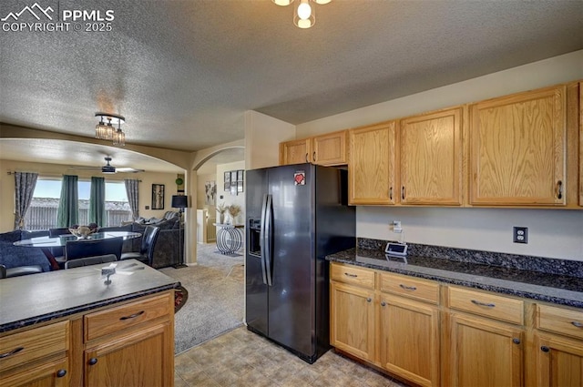 kitchen featuring black fridge with ice dispenser, light colored carpet, a textured ceiling, ceiling fan, and dark stone counters