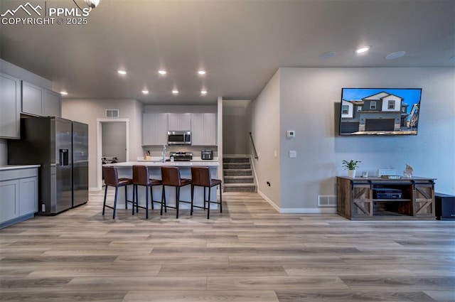 kitchen with white cabinets, an island with sink, a breakfast bar, stainless steel appliances, and light countertops